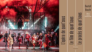 Auf der Bühne singt eine Frau am Mikrofon, während alle Schauspielerinnen und Schauspieler dem Publikum zugewandt sind. Einige tanzen, andere sitzen auf einer Treppe und schauen ins Publikum. Kabarett-Atmosphäre und roter Rauch. Rechts im Bild ist das Buchcover der neuen Übersetzung der Dreigroschenoper zu sehen.