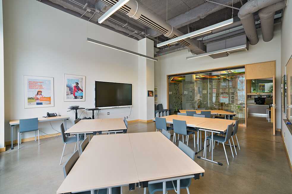 A classroom setup displaying tables and chairs facing a large screen, prepared for teaching and student engagement.