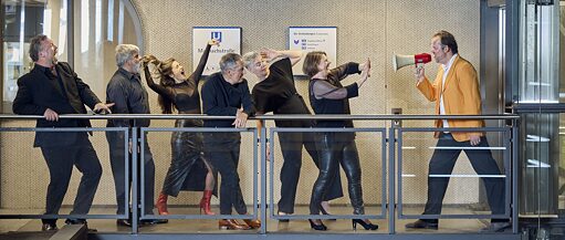 Yedi kadın ve erkekten oluşan bir grup, bir metro istasyonu tabelasının önünde sıra halinde durmaktadır. Altısı da el hoparlöründen konuşan bir adama bakmaktadır