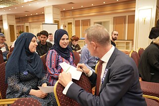 Zwei junge Frauen üben mit dem Generalkonsul die deutsche Sprache.