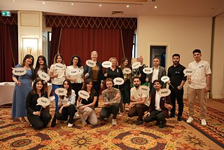 Eine Gruppe Menschen hält Probs mit Grüßen in verschiedenen Sprachen hoch