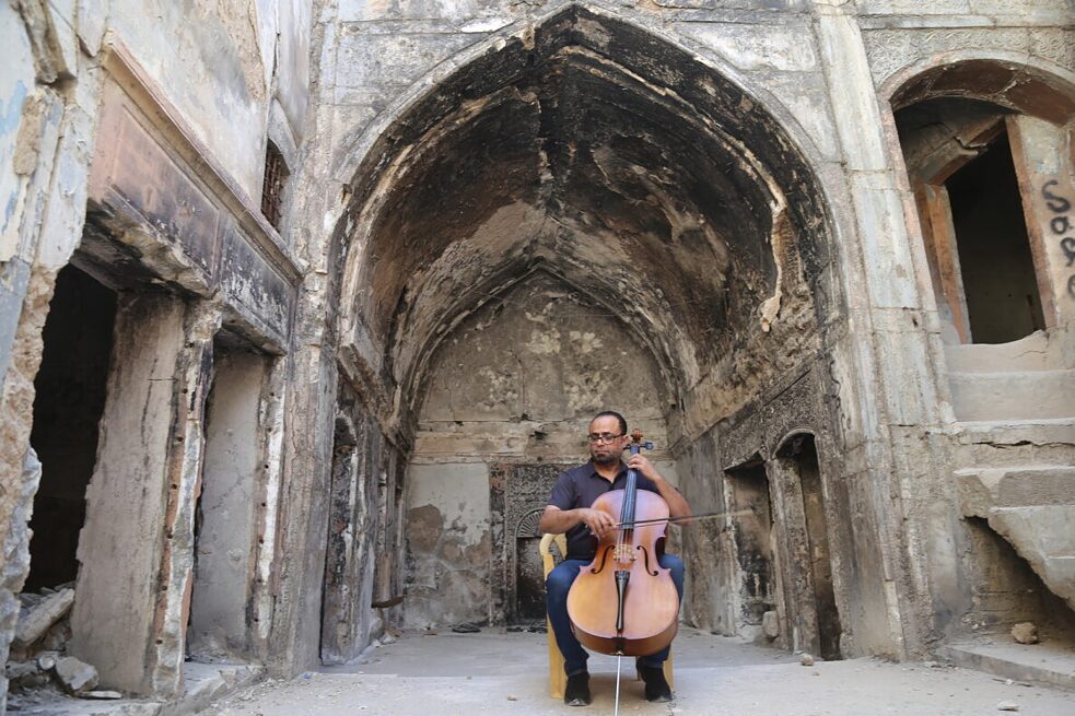 Ein Mann spielt Cello vor einem zerstörten Gebäude in Mosul