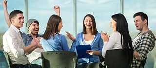 6 Menschen sitzen lächeln und klatschend um einen Tisch