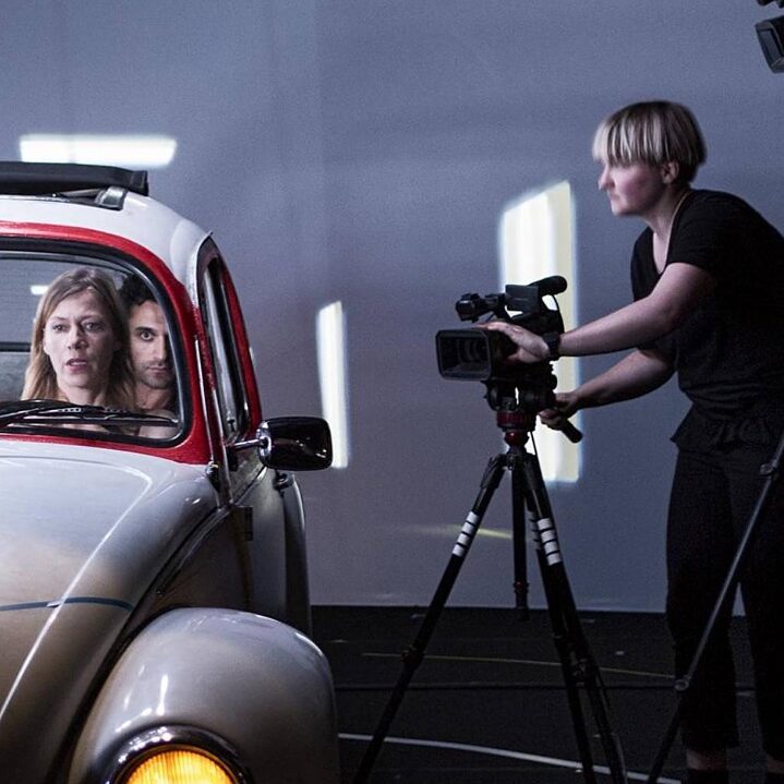 A pla takes place onstage. Actors sit inside a car while being filmed from outside the car.