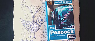 Das Buch 'The Peacock' liegt auf einem besticktem weißen Kissen