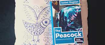 Das Buch 'The Peacock' liegt auf einem besticktem weißen Kissen