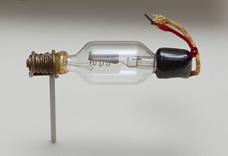 Eine frühe De-Forest-Audion-Röhre, die erste Elektronenröhre, die verstärken konnte. Die erste Triodenröhre, d. h. eine Röhre mit drei Elektroden, einem Glühfaden, einem Gitter und einer Platte, wurde 1906 vom amerikanischen Ingenieur Lee De Forest erfunden. Die obere Metallelektrode ist die Platte. Der zickzackförmige Metalldraht, der teilweise darunter sichtbar ist, ist das Gitter. Ursprünglich befand sich darunter der Glühfaden, der an den Drähten links befestigt war, aber durchgebrannt ist. Wie viele Audions hatte auch dieses Modell zwei Glühdrähte (erkennbar an den vier Drähten für die Glühdrahtversorgung), so dass der "Ersatzdraht" verwendet werden konnte, wenn einer durchgebrannt war. Die Glühdrähte wurden an der Schraubklemme links angeschlossen, während die Anschlüsse für das Gitter und die Platte durch das rechte Ende des Glaskolbens zu den beiden Drähten rechts herausgeführt wurden. Die Röhre gehört zur Geschichte von San Jose, Perham Collection of Early Electronics.