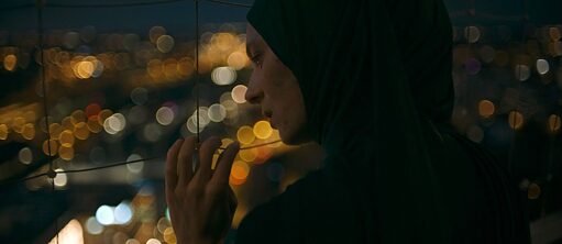 A woman in profile looking down over blurred city lights