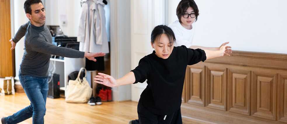 three dancers with arms open wide move in unison across the floor