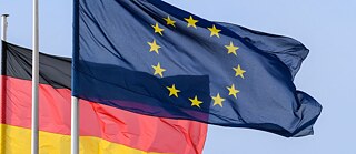 Les drapeaux allemand et européen flottent dans un ciel bleu.