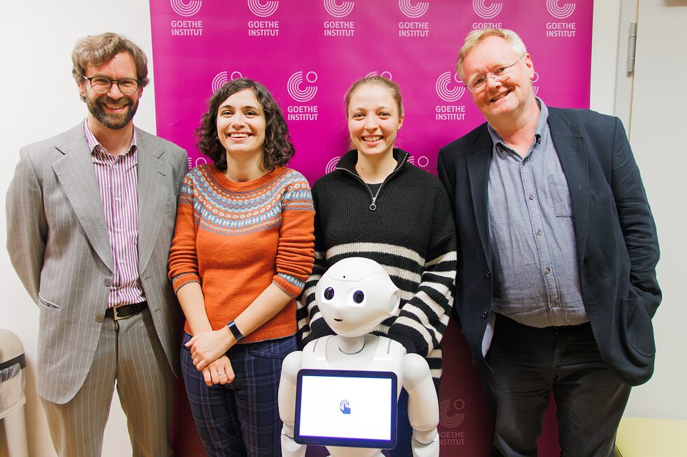 Christophe Fricker, Ayça Türkoğlu, Janiça Hackenbuchner und Jamie Bulloch posieren mit GILON, dem Bibliotheksroboter im Goethe-Institut London