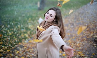 Eine Frau tanzt mit ausgebreiteten Armen in fallendem Laub