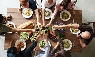 Menschen von oben fotografiert sitzen an einem gedeckten Tisch und stoßen mit ihrem Getränk an.