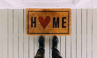 Füße stehen vor einer Türmatte mit der Aufschrift "Home".