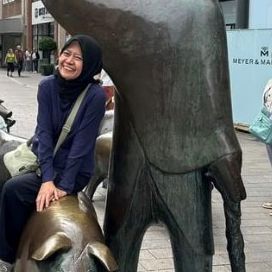 Narmawarni Abdul Kadir sitzt auf einen Brunnen in einer Fußgängerzone und lacht. © Narmawarni Abdul Kadir Narmawarni Abdul Kadir