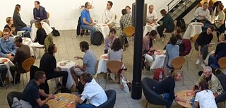 Dreiergruppen die um Tische sitzen und diskutieren