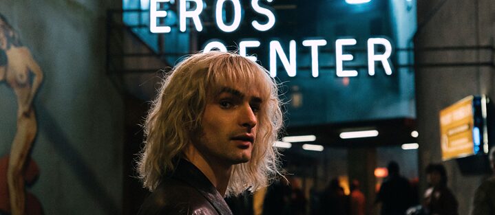 Still image from the Amazon Original series "Luden Kings of the Reeperbahn" shows the title character Klaus Barkowsky portrayed by Aaron Hilmer in front of an Eros Center.