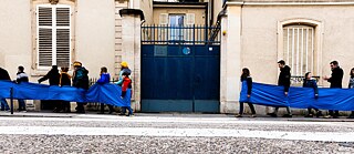 Eine Reihe von Menschen läuft, verbunden durch ein blaues Tuch,  durch die Straßen