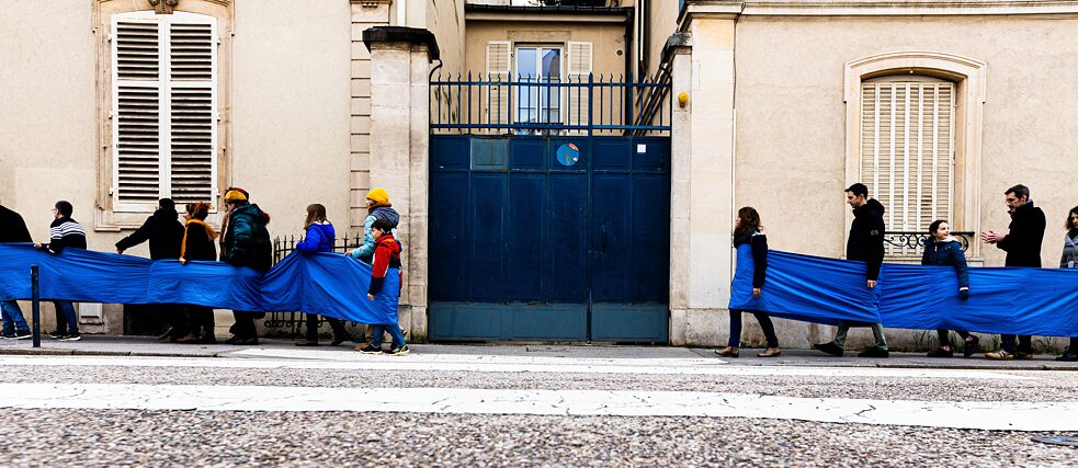 Une série de personnes marchent dans les rues, reliées par un tissu bleu