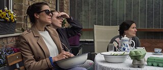 Τρεις γενιές γυναικών κάθονται μαζί έξω, κοιτάζοντας όλες προς την ίδια κατεύθυνση.