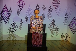 Clay sculpture surrounded by diamond shaped objects hanging from the ceiling