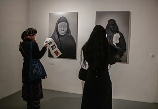 Two black and white photographs each depict two women whose bodies are covered with lettering