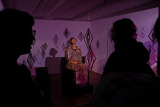 Two visitors are shown with their backs to the camera, looking at a sculpture in a darkened room