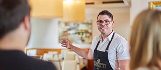 Person in Restaurantumgebung zeigt mit der Hand, trägt eine Schürze 
