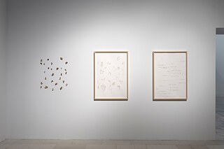 Pottery mosaics on a white wall, next to two frames with pencil drawings