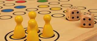 Spielbrett des Spiels "Mensch ärgere dich nicht" mit vier gelben Figuren und zwei Würfeln. 