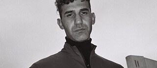 Bogaktuelle Necati Öziri gæster online-eventserien Meet the Author den 19. marts. Necati Öziri ser ned i kameraet; himlen og en lille del af et højhus kan ses i baggrunden. 