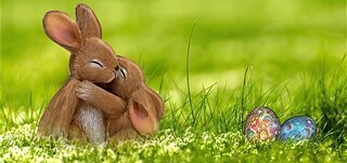 Two Easter bunnies hug each other in the green grass and two colorful eggs lie next to them.