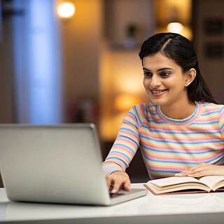 Eine junge Frau sitzt zu Hause am Laptop und lernt.