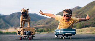 Ein Junge fährt liegend auf einem Skateboard, er streckt die Arme wie ein Flugzeug von sich