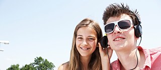 Eine Jugendliche und ein Jugendlicher sind auf der Straße mit Kopfhörern und lächeln in die Kamera