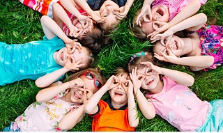 Un grupo de niños y niñas están de manera circular tumbado en un pradero