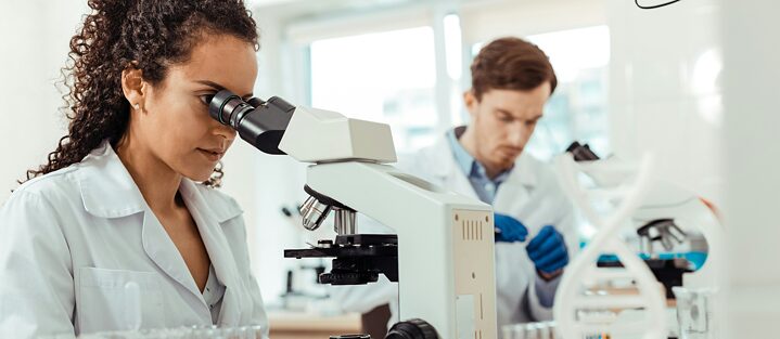 a scientist in a white coat looks into a microscope