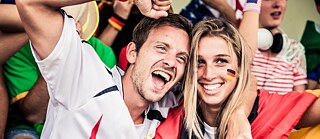 A man in a fan shirt and a woman with a Germany jersey draped over their shoulders lie in each other's arms and cheer.