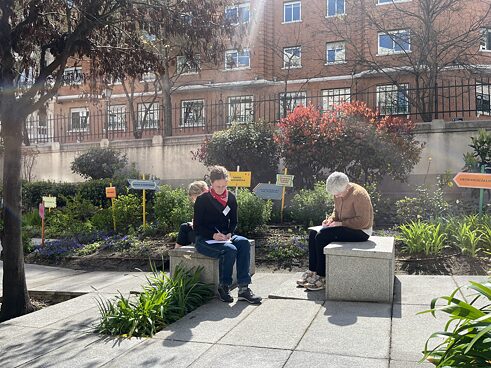 L@s participantes estan sentad@s en el patio escribiendo sus propios textos. 
