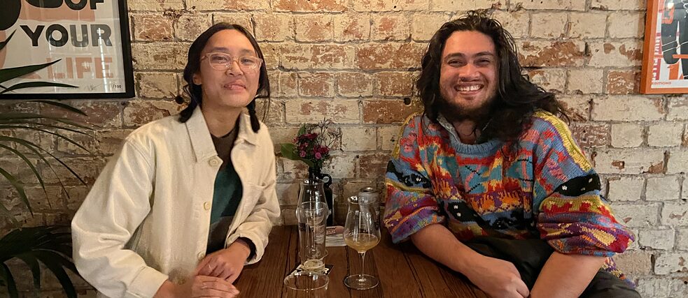 The Friends of Goethe Australia Scholars of 2023 Isabella Alvarades and Andy Butler sit at table in a bar and celebrate their success.