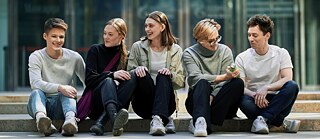 Eine Gruppe junger Erwachsenen sitzen auf einer Treppe draußen ©   Deutsche Sprache