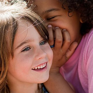 Zwei Kinder flüstern sich etwas zu und lachen.