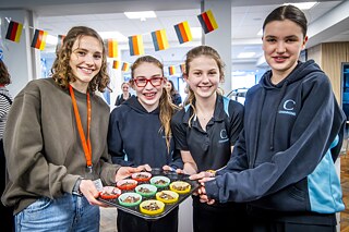 Gruppe von Mädchen im Alter 10-13 mit bekannter Bloggerin FitGreenMind,  sie halten ein Blech mit Muffins, die bald in den Ofen kommen