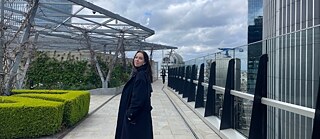 Julia steht in einem Mantel auf dem Dach einer Gärtnerei.