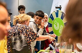 Junge mit Frau stehen vor einem Glücksrad und besprechen sich