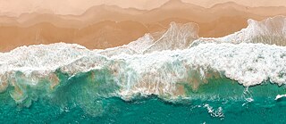 Wellen eines Ozeans, die an den Strand rollen fotografiert von oben   
