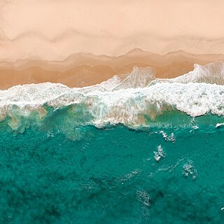 Wellen eines Ozeans, die an den Strand rollen fotografiert von oben   