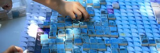 Kinderhände arbeiten an einer blau-bunten Mosaik
