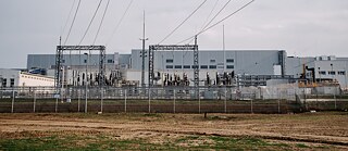 Photo is showing large grey factory buildings with high-voltage cables. 