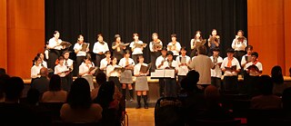 Ein Chor aus PASCH Schüler*innen und Chorleiter Yoshihisa Matthias Kinoshita treten auf vor einem Publikum